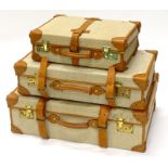 A graduated set of three canvas and brown leather vintage suitcases, the largest 73cm wide, smallest