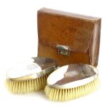 A pair of George V silver mounted brushes, each engaged with a monogram and in a leather carrying