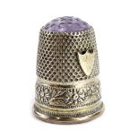 A small white metal thimble, engraved and cast with flower heads, vacant cartouche and with a purple