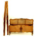 An early 20thC French beech and caned bergere bed head and foot, with a moulded frame carved with