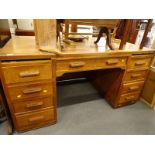 A large oak kneehole desk, with nine drawers on plinth base.