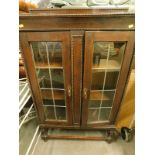 A 1920s oak bookcase, with beaded outline and lead glass panelled doors on turned legs joined by