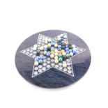 A Taiwanese black marble solitaire board, with glass marbles, board 30.5cm diameter.