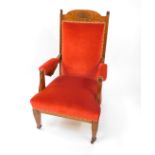 A Victorian lady's oak framed armchair upholstered in overstuffed red draylon, raised on tapering