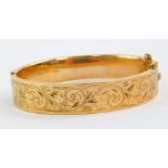A 9ct gold bangle, foliate engraved, on a snap clasp, with safety chain as fitted, 18.4g.