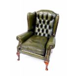 An oak and green leather button back wing armchair, raised on cabriole legs.