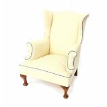 A mahogany framed wing armchair, upholstered in patterned cream fabric, with blue piping.