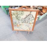 An oak framed fire screen with wool needlework panel of a cottage.