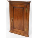 An 18thC oak hanging corner cupboard, of shaped form with panel door and brass hinges on a plain