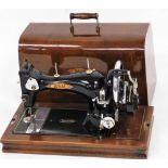 An early 20thC Triumph manual sewing machine, in black on oak stained base, with cover, 36cm wide.