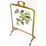 An early 20thC brass framed fire screen, with painted glazed centre set with flowers on shaped