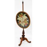 A Victorian walnut pole screen, with oval floral woolwork panel, and tripod base.