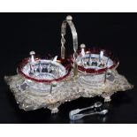 A silver plated sweet meat basket, set with two red and clear glass dishes, on a shaped repousse