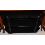 A glass three tier television stand, in black colour way, with chrome finish trim.