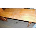 A large rectangular pine kitchen table, on turned legs.