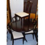A dark wood circular extending dining table and four Hepplewhite style chairs, with pierced back