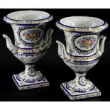 A pair of continental porcelain two handled urns, each decorated with flowers, within gilt borders,