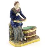 A late 19thC continental majolica match holder, modelled in the form of a lady seated with a basket