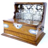 A late 19th/early 20thC oak and silver plated tantalus, with three square section decanters, a hinge