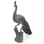 A bronzed metal peacock garden ornament, in oriental style, standing on a tree stump, 86cm high.