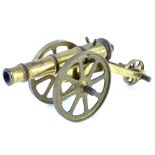 A miniature brass cannon, on a three wheel brass carriage with spoked wheels.