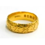 A 22ct gold embossed wedding band, with design of leaves and flowers, of hammered design, ring size