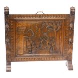 A late 19th/early 20thC oak fire screen, carved centrally with a village scene with windmill, figure