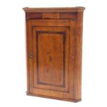 An early 19thC oak and mahogany crossbanded corner cabinet, with a single panelled door inlaid with