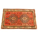 A Persian rug, with a central pole medallion in blue, on a red ground with multiple borders, 79cm x