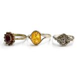 Three silver dress rings, comprising an amber set dress ring, a marquasite set dress ring and a clus