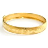 A hinged bangle, with polished design with scroll decoration of leaves, yellow metal, marked 18ct,