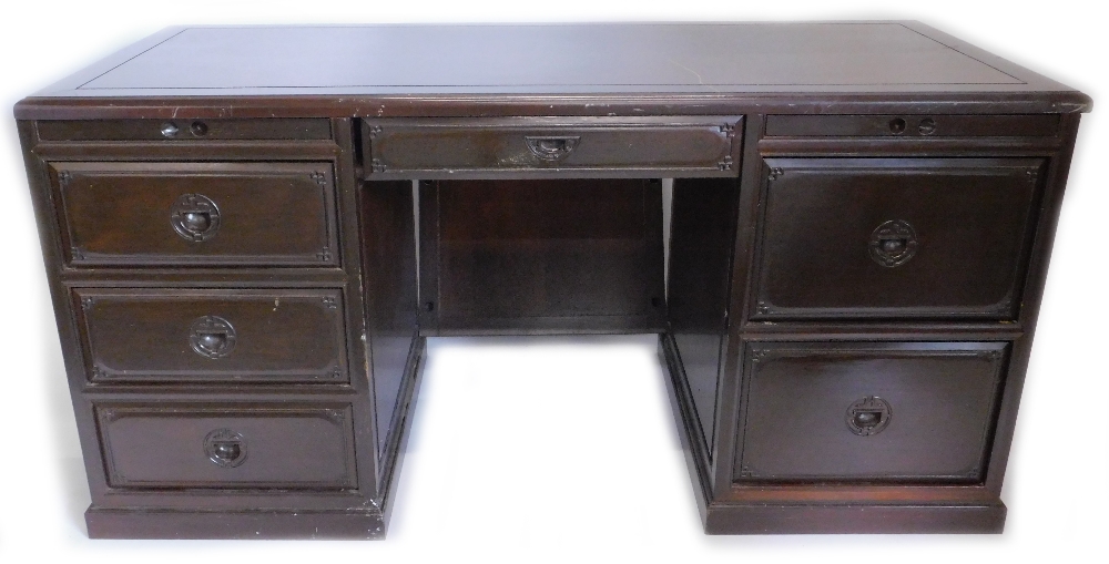 An oriental hardwood kneehole desk, with an arrangement of drawers and slides etc, on a plinth base,