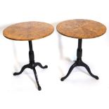 A pair of burr elm and ebonised occasional tables, each with a circular tilt top, turned column and