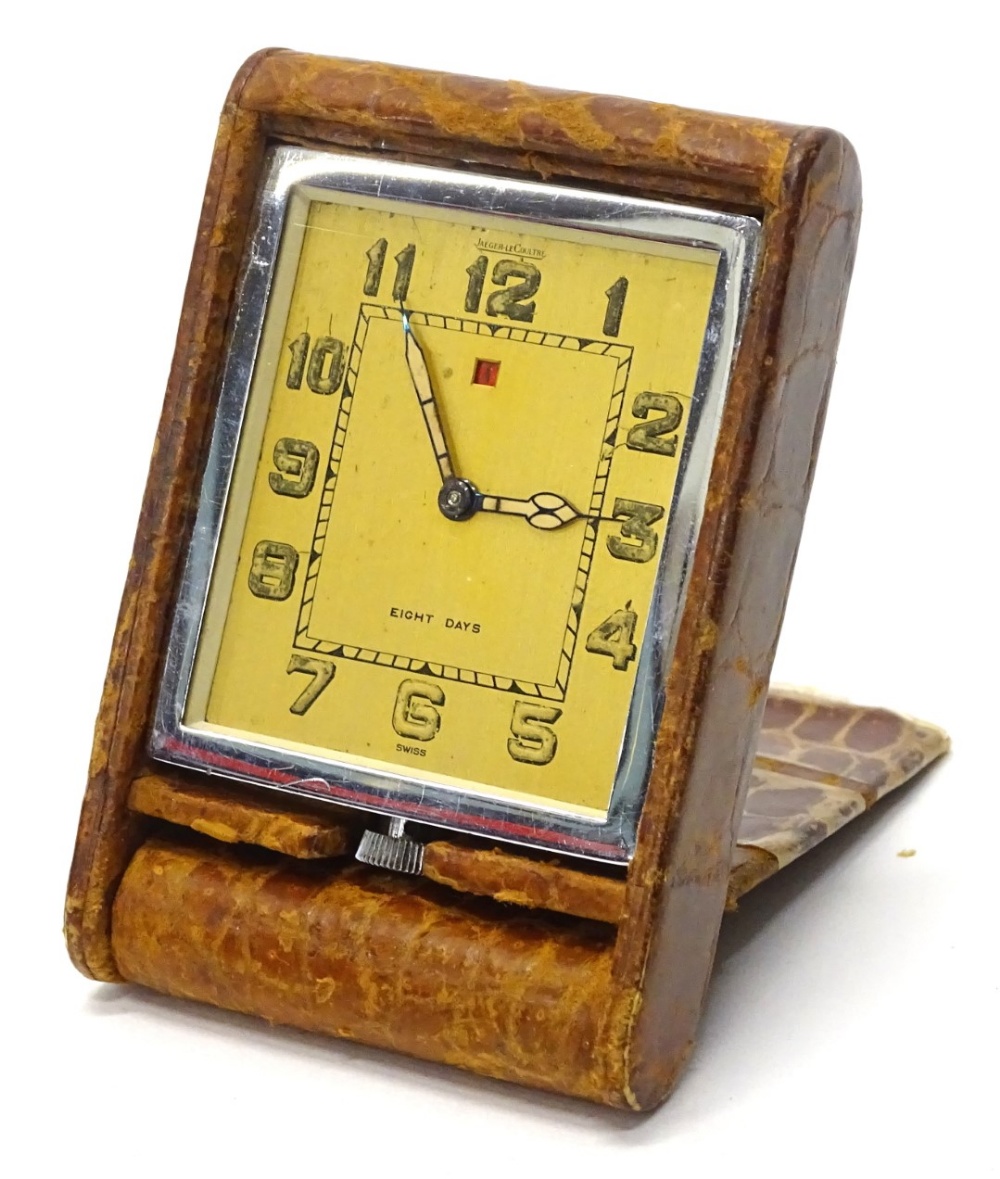 A Jaeger Le Coultre travel clock, with a gold dial, a red date apeture, with a chrome and leather ou