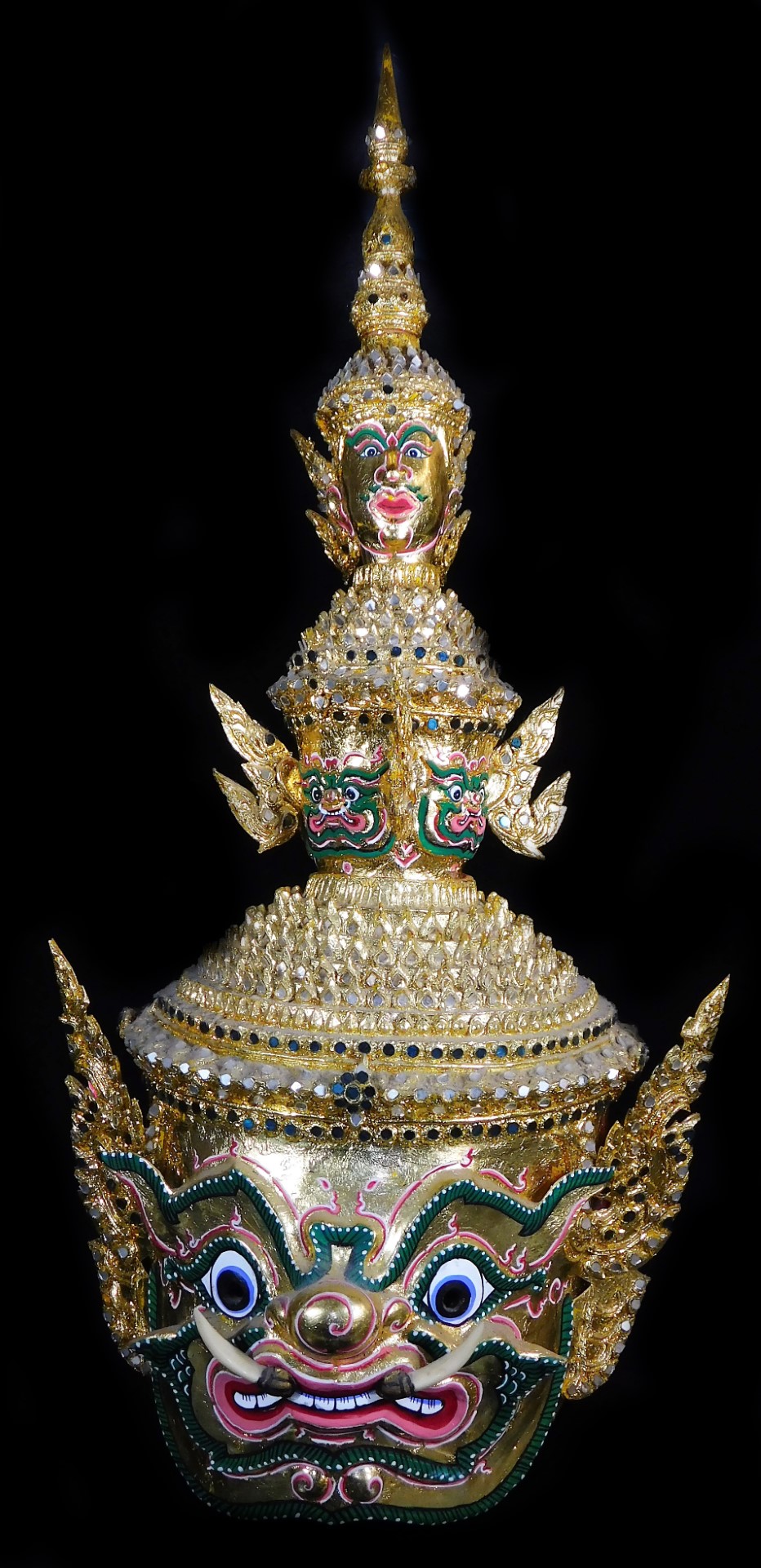 A Thai face mask, heavily decorated with mirrored glass sections set with tusks and with fierce