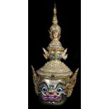 A Thai face mask, heavily decorated with mirrored glass sections set with tusks and with fierce
