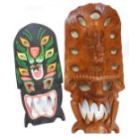 Two various hardwood wall masks, to include one profusely decorated on a black ground, 65cm high. (