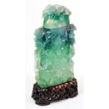 A Chinese green quartz vase and cover, heavily carved with flower heads, on a carved wood base,