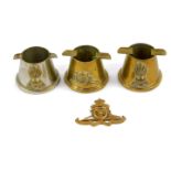 Three Royal Artillery trench art metal ashtrays, together with a Royal Artillery cap badge. (4)