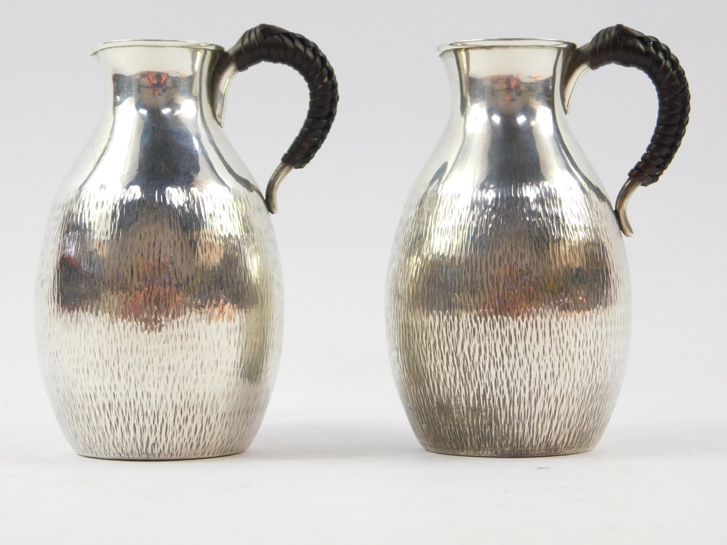 A pair of Japanese silver jugs, with leather bound handles, of bulbous form, with textured