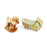 A Staffordshire early 19thC pearl ware cradle, 10cm wide, together with a slip ware figure of a dog,