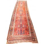 A Caucasian red ground runner, decorated with a geometric and floral repeating motifs, within floral