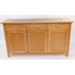 A light oak sideboard, the top inset with black glass, over three drawers above cupboard doors,