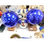 Three glass witches balls, two in cobalt blue, the other in silver.