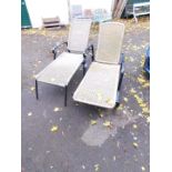 A pair of black metal and woven plastic garden loungers.