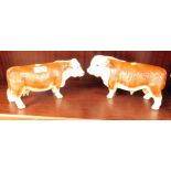 A pair of mid 20thC pottery figures modelled as a bull and cow, 24cm wide.