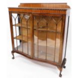 A 20thC mahogany serpentine display cabinet, the carved top raised above a pair of astragal glazed d