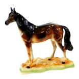 A late 20thC pottery model of a bay horse, standing on a naturalistic base, unmarked, 39cm high.
