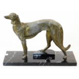 A 20thC bronze finish figure of a standing lurcher, on a marble finish base, with right leg on a ste