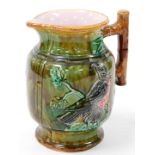 A late 19thC Majolica jug, with beak spout and bark handle, the main body raised with birds on a gre